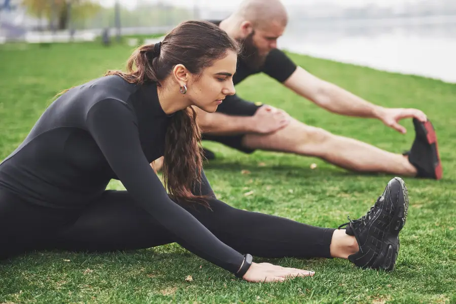 Fitness couple stretching outdoors in park near the water. Young bearded man and woman exercising together in morning